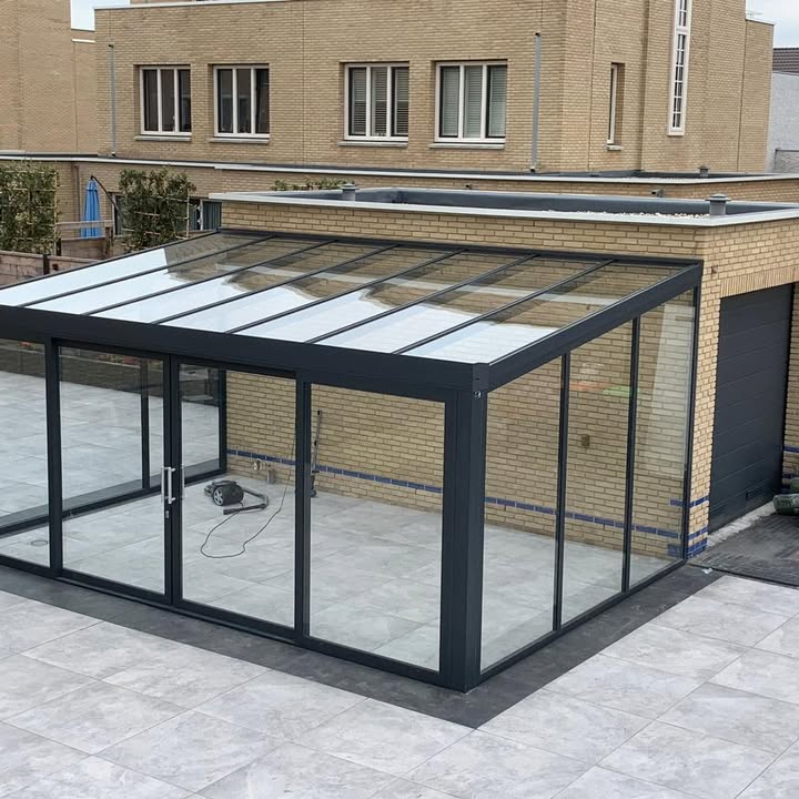 Glazen kamer met een dak van glas en glazen schuifwanden op een betegeld terras