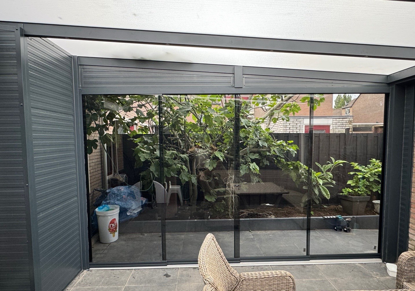 Glazen schuifwand met dichte aluminium zijwand, uitzicht op de tuin met een vijgenboom