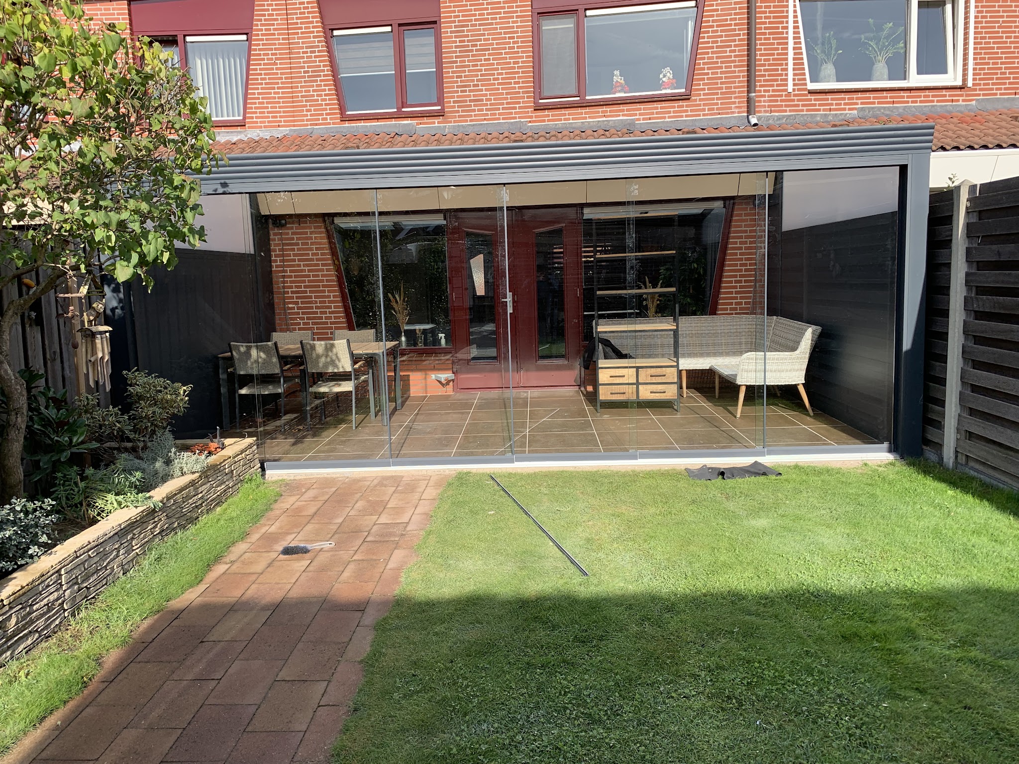 Afgewerkte antraciet veranda met glazen schuifwanden over het terras van een rijtjeshuis, met tuinmeubels eronder